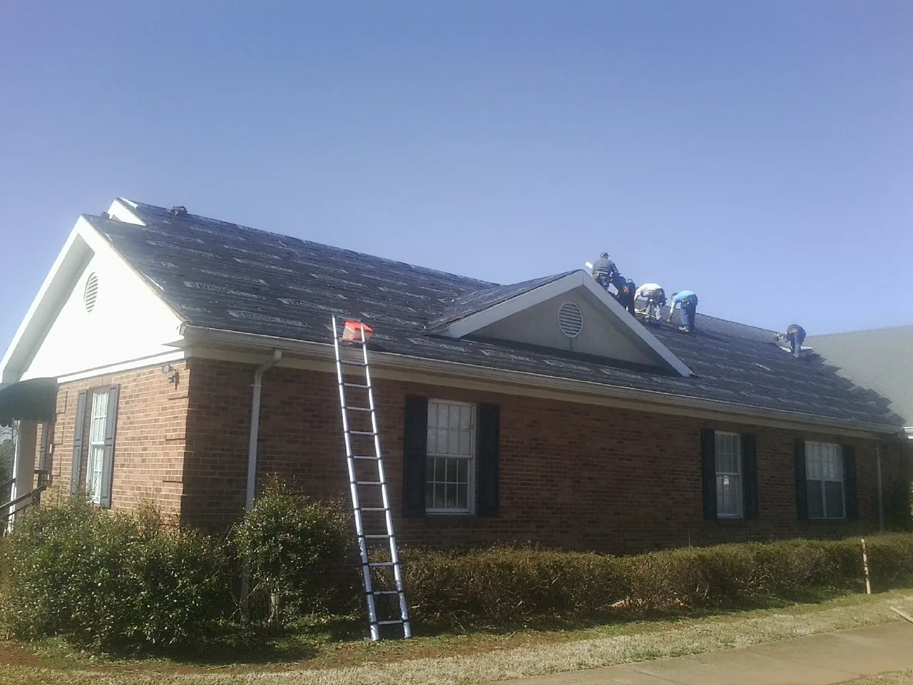 Crew tearing shingles off a brick ranch roof with a ladder set — Emergency Roof Repair work by our crew in Cornwall On Hudson