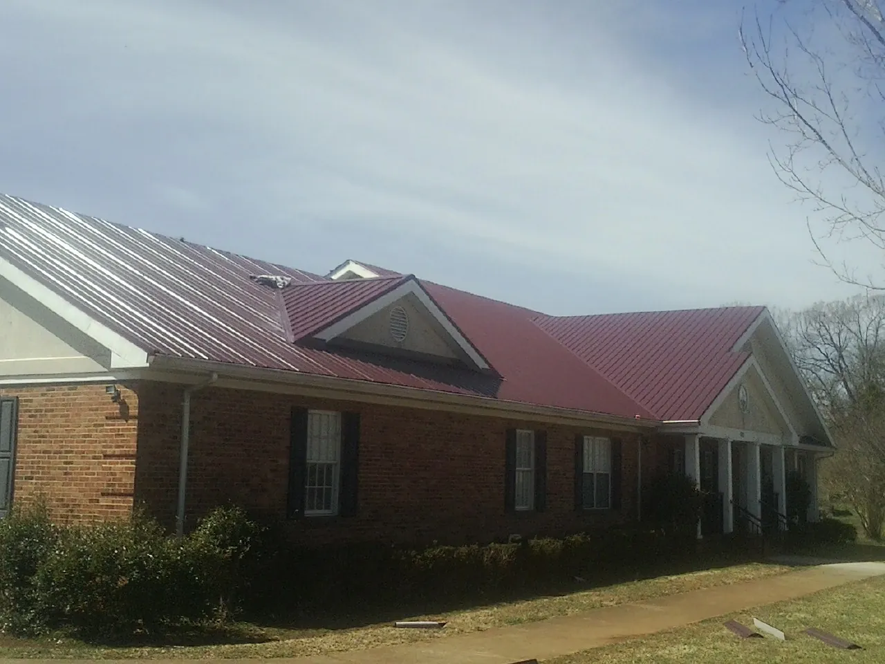 Red metal roof with gabled entries on a long brick building, from a Hail Damage Roof Repair job in Cornwall On Hudson