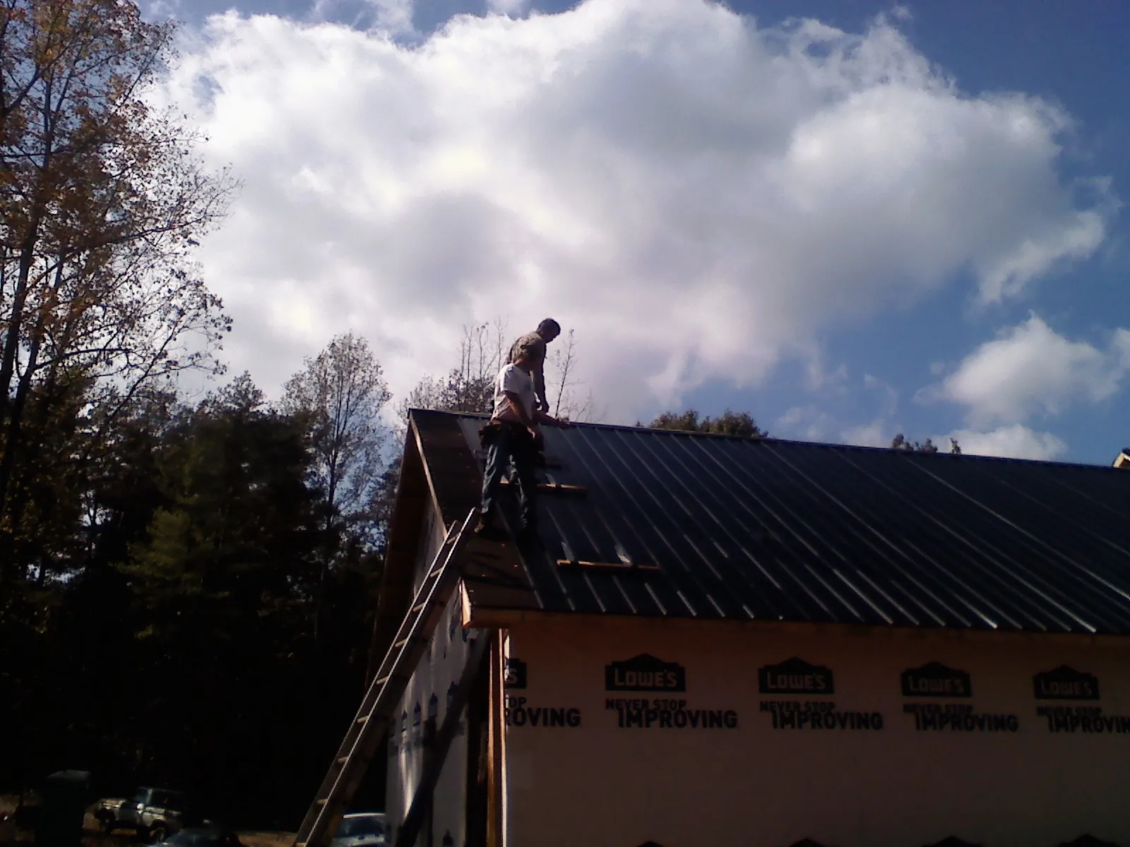 Roofer fastening dark metal panels high against a cloudy sky, from a Roof Inspection job in Cornwall On Hudson