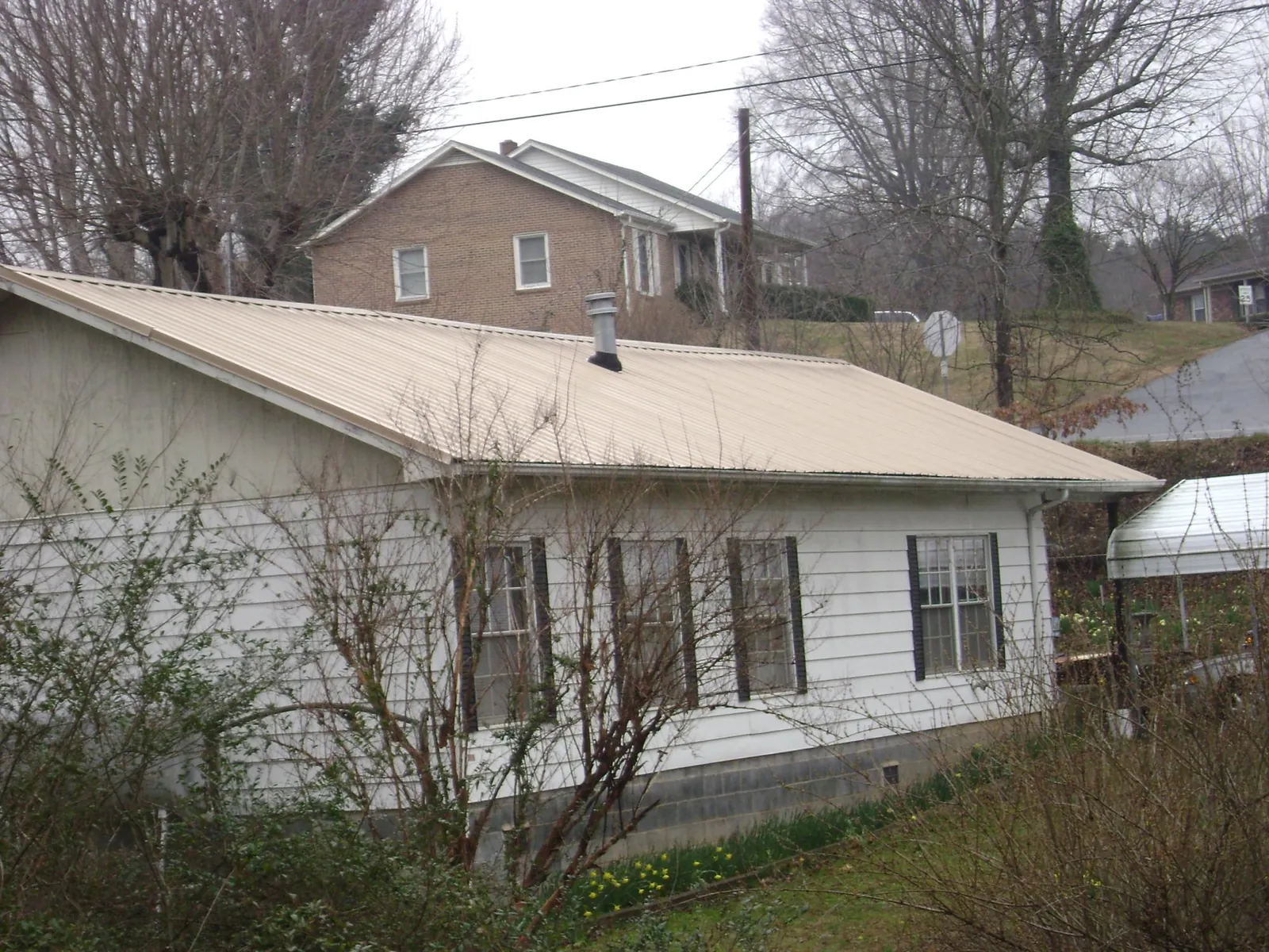 Tan metal roof on a white sided house set into a hillside — Commercial Roofing by Roofing Brothers in Cornwall On Hudson